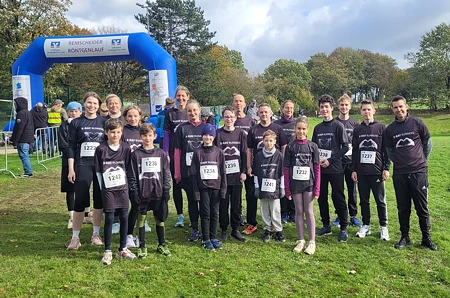 Eine Gruppe von Läufer:innen in Sportkleidung steht auf einer Wiese vor einem blauen Startbogen.